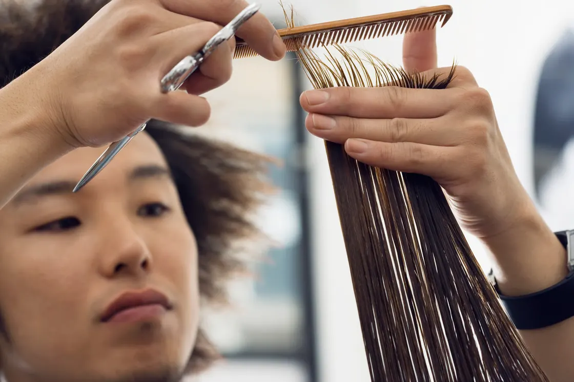 Stylist cutting a section of long hair held between comb and fingers