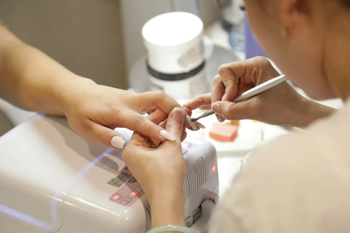 Nail technician doing a manicure next to a UV nail lamp