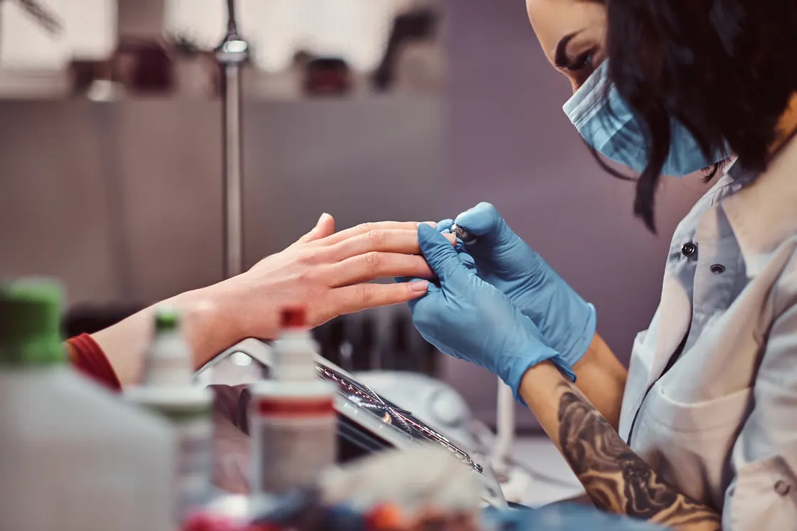 Nail technician in a mask filing a client's nails