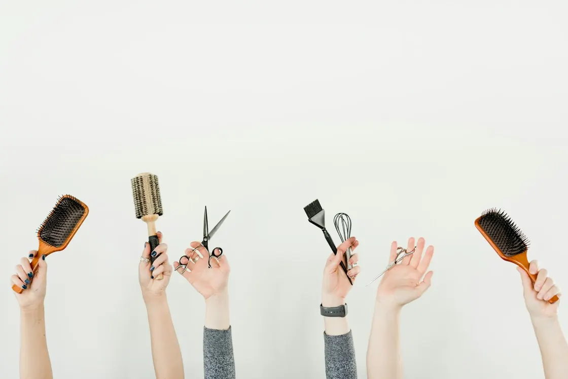 Hands holding hairbrushes, scissors and a tint brush for beauty training